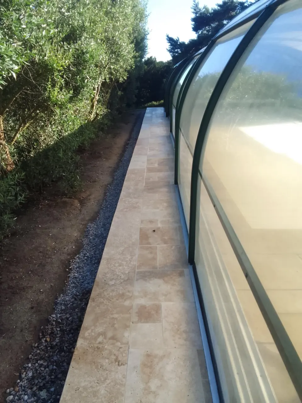 Allée en travertin posée le long d'une verrière de piscine